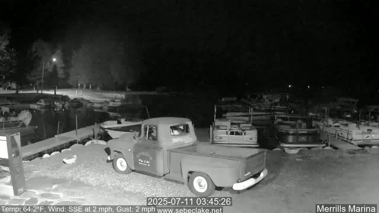 A vintage pickup truck is parked at a marina at night, under a dark sky with a light south-southeast wind.