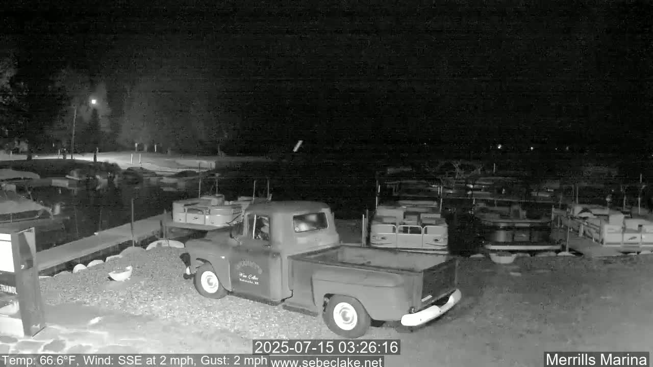 A red pickup truck is parked at night in a marina with numerous boats docked under a dark, clear sky.