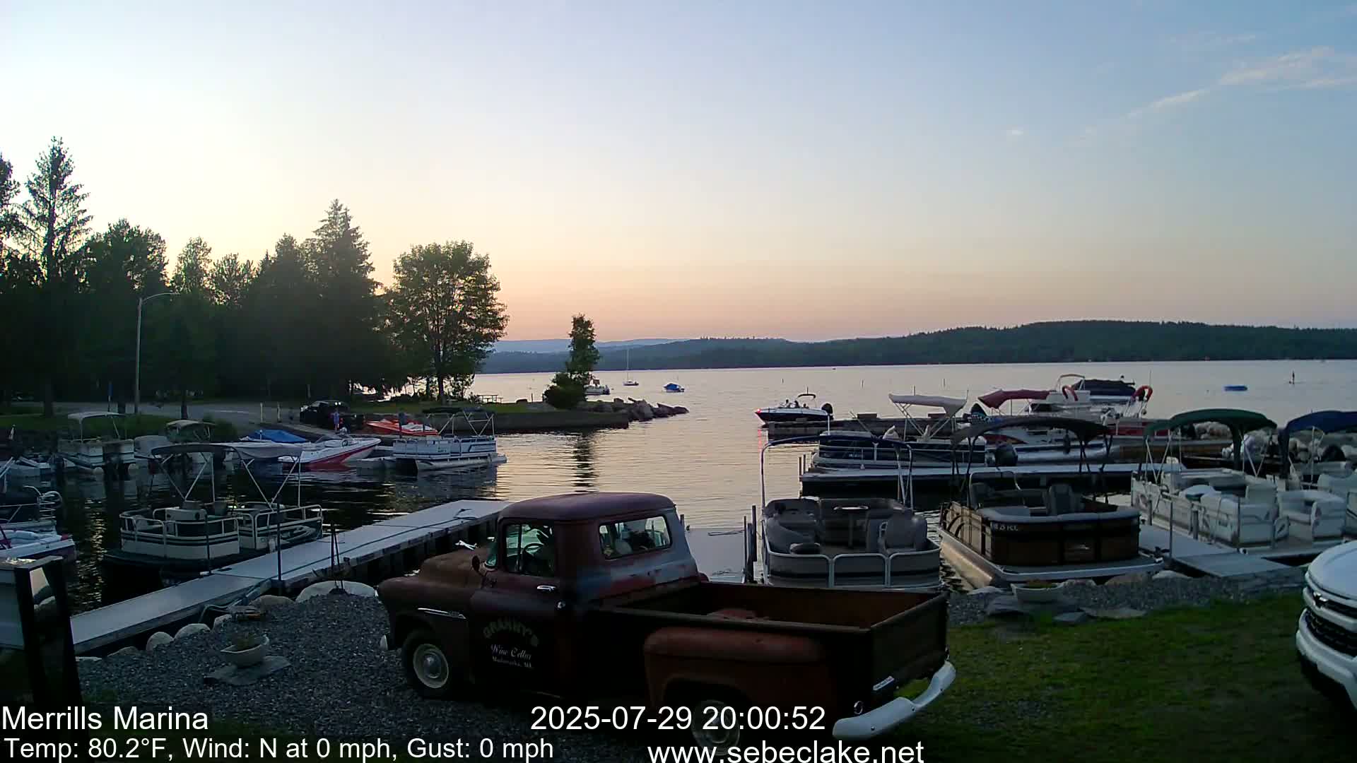 A nighttime, low-light grayscale image shows a vintage pickup truck parked in a marina with numerous boats docked nearby under a dark, clear sky.