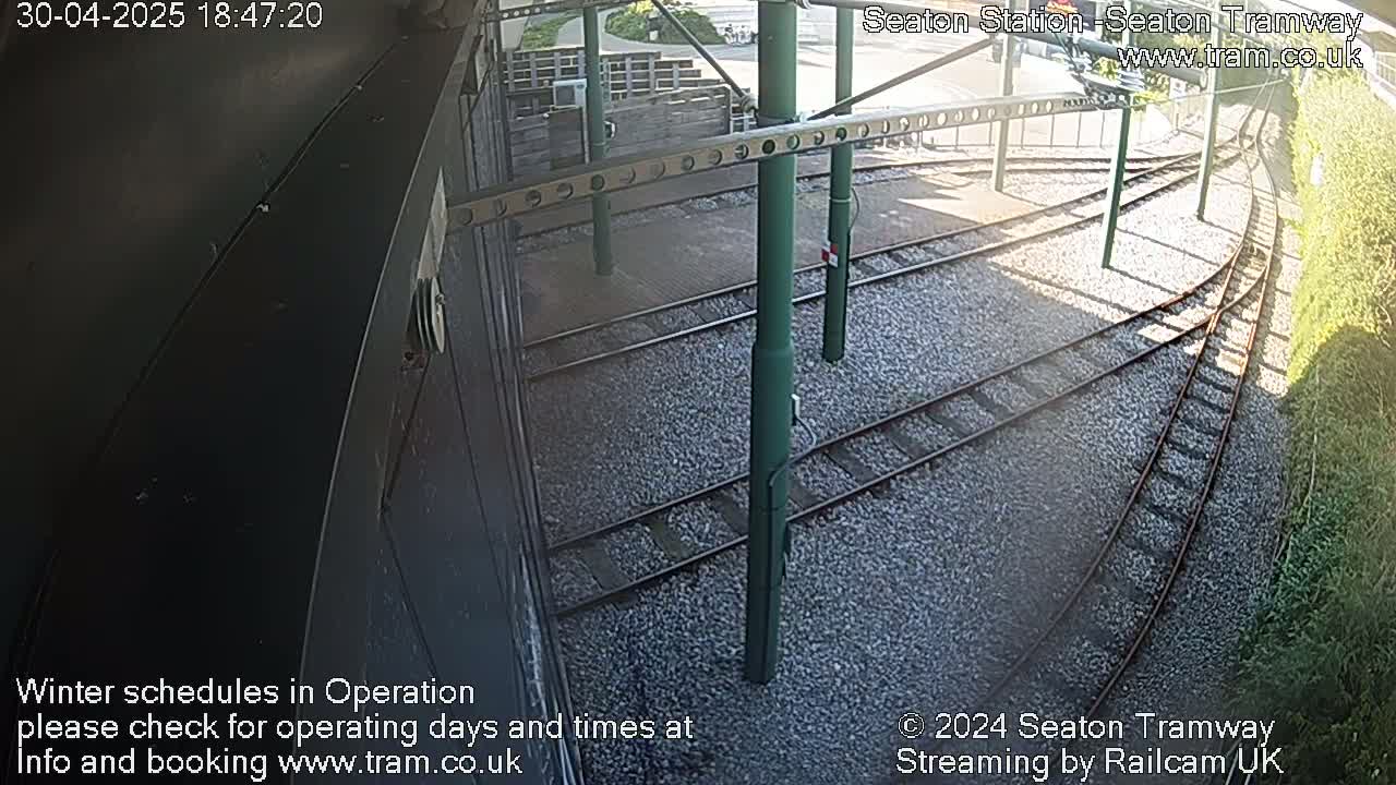A high-angle view of several tram tracks curving to the right, set in gravel, partially shaded by a structure.