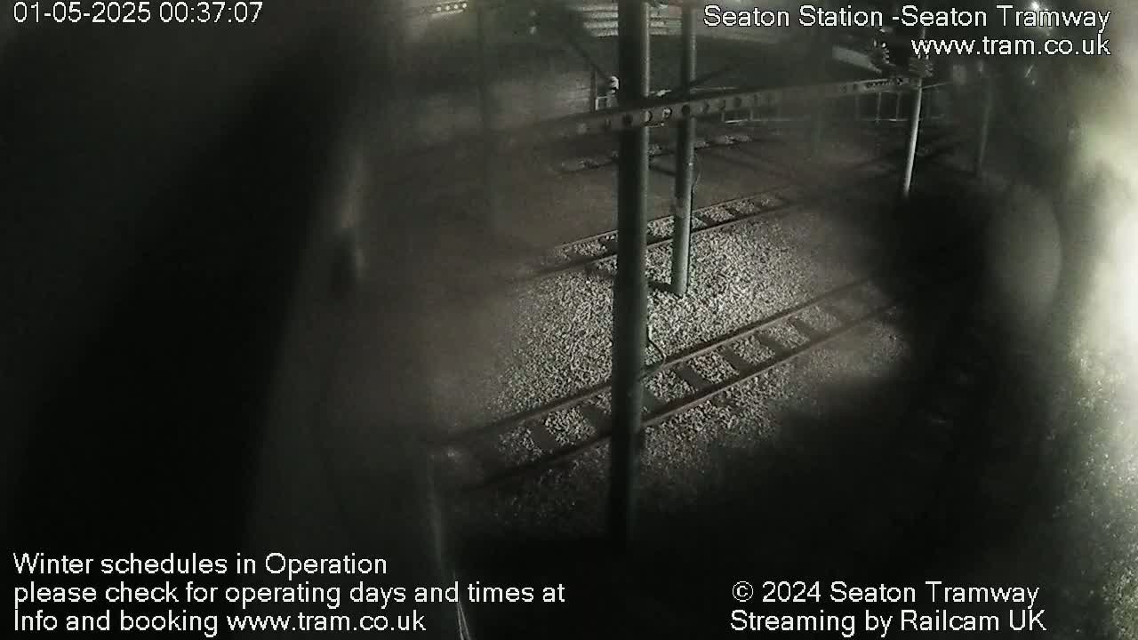 A nighttime, overhead view of train tracks covered in gravel, with metal support structures visible.