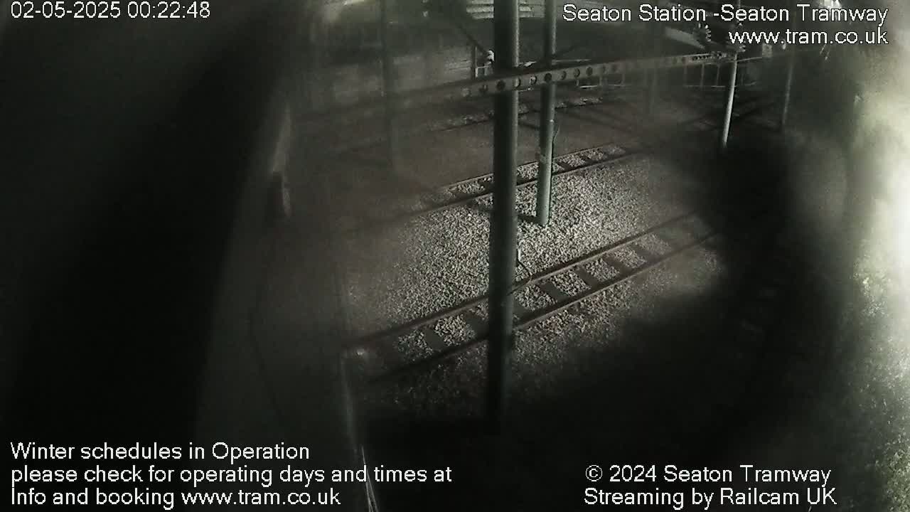 A nighttime, overhead view of train tracks covered in gravel, under a dark structure.