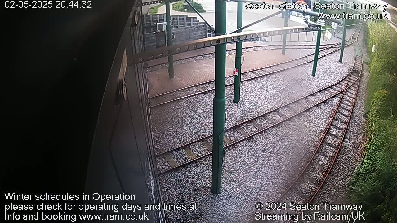 A view from a tram shows several train tracks curving around a station platform covered in light-colored gravel.