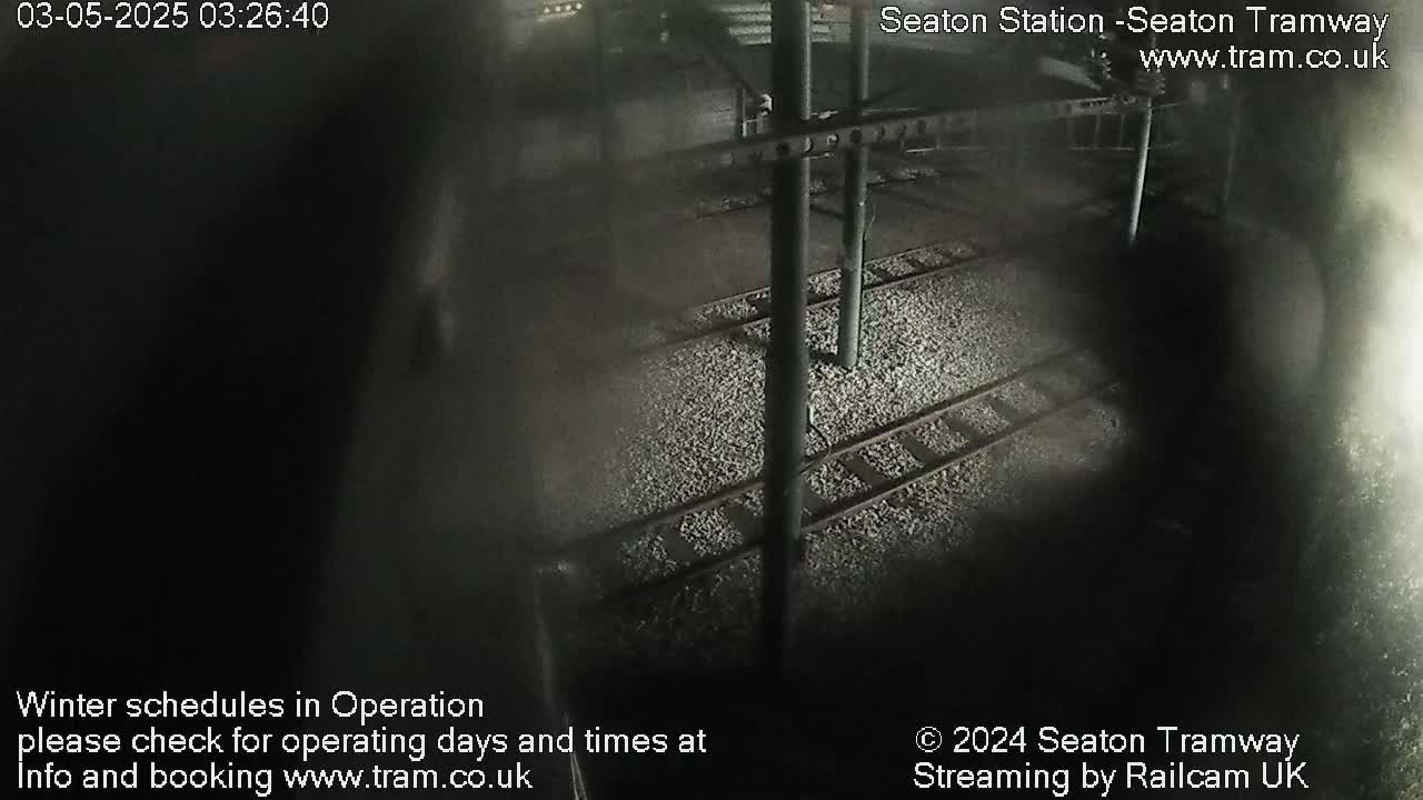 A dark, nighttime view of train tracks covered in light-colored gravel, under a structure.