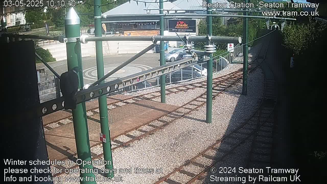 A sunny view of tram tracks and a station, with several cars parked nearby.