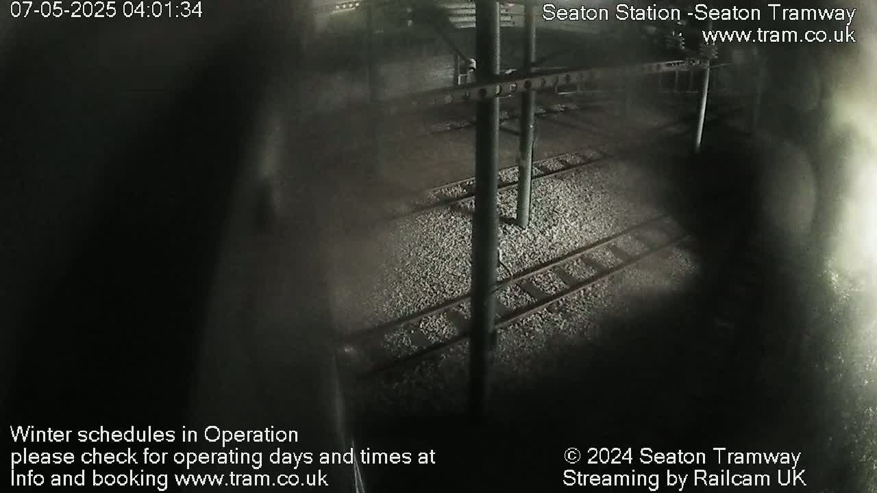 A nighttime, dimly lit view of train tracks and supporting structures at a station.
