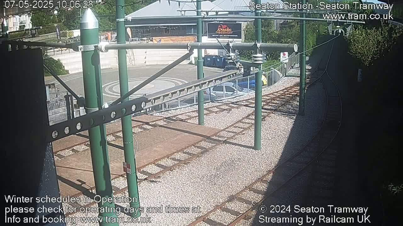 A sunny overhead view of tram tracks curving through a station area with several cars parked nearby.