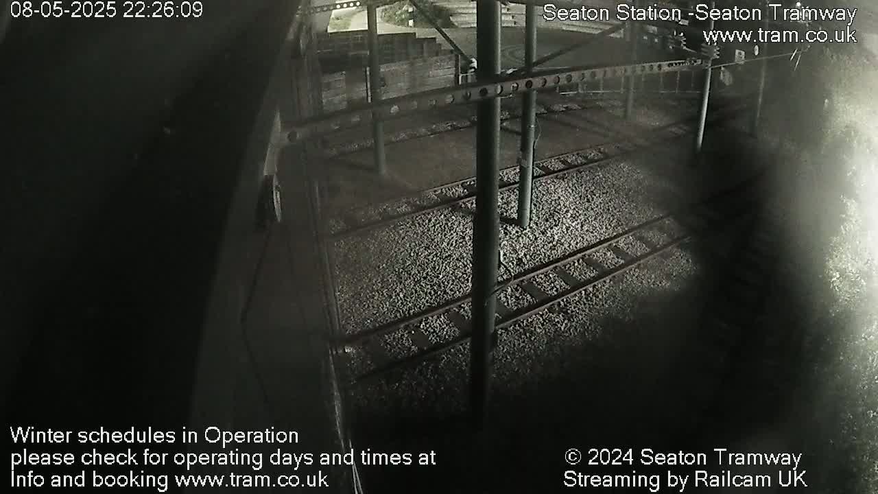 A nighttime, overhead view shows train tracks covered in light-colored gravel.