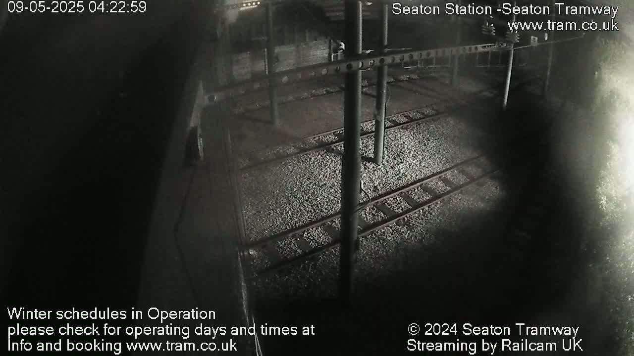A nighttime, overhead view of train tracks covered in gravel, beneath a dark structure.