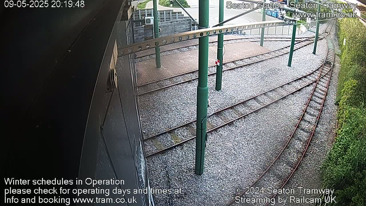 A high-angle view shows railway tracks and supporting structures at a station, covered with small stones.