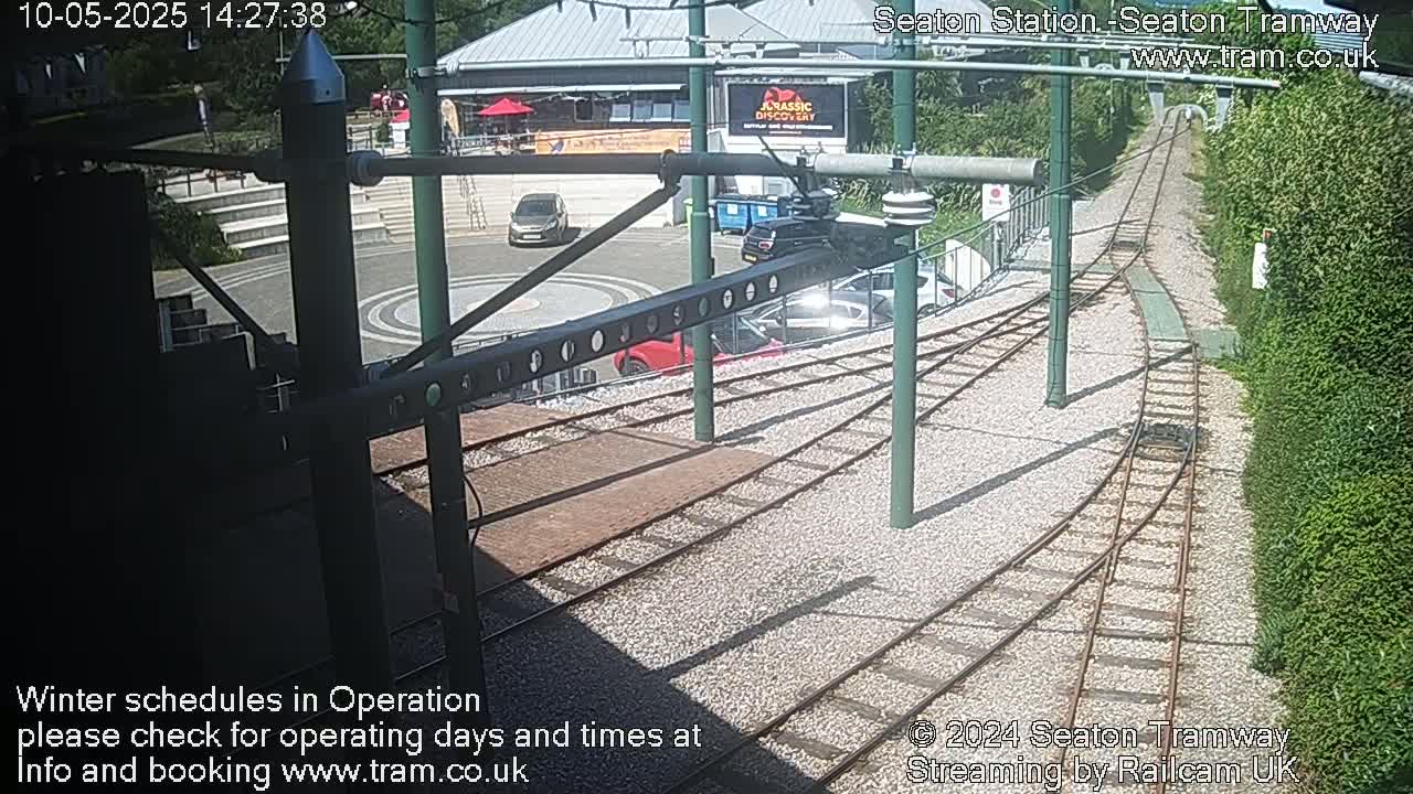 A sunny outdoor view of tram tracks curving around a station area with several parked cars and a building in the background.