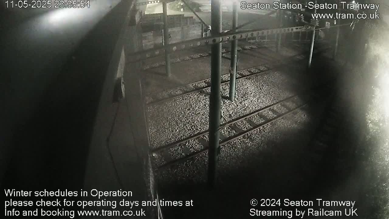 A nighttime overhead view of train tracks and a station platform, partially obscured by shadow.