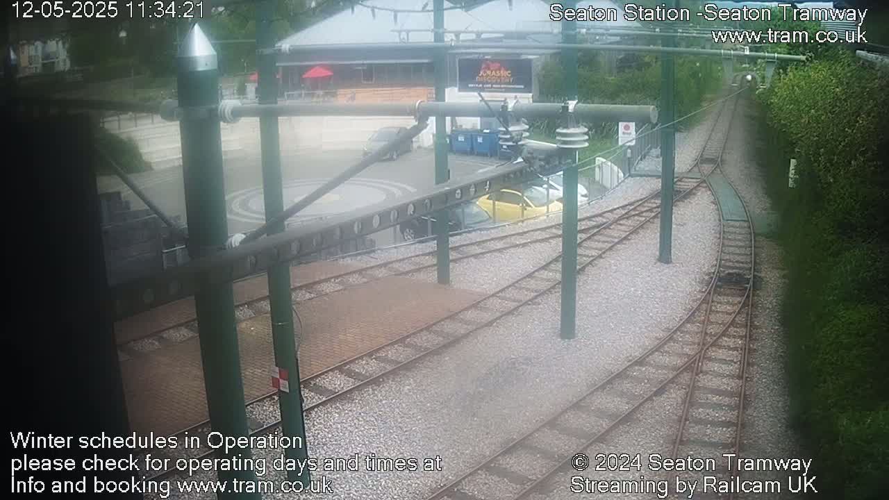 Tram tracks curve through a station area with several parked cars and a building visible in the background on an overcast day.