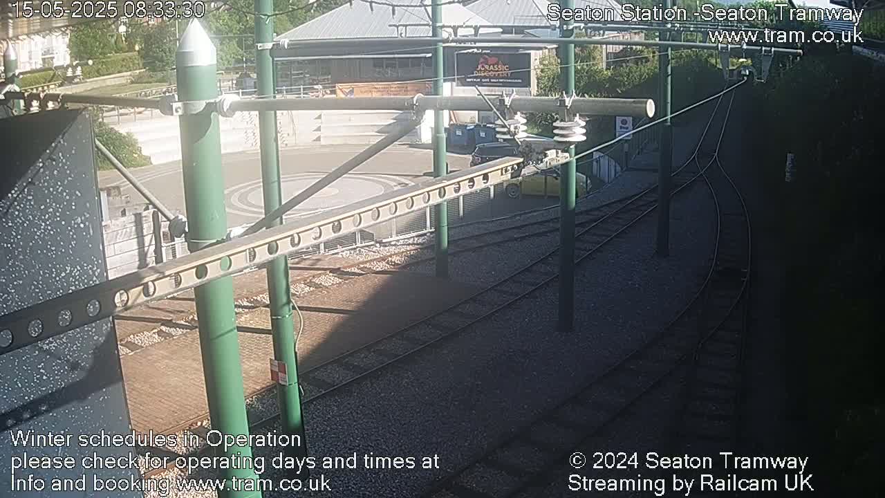 A sunny view of a tram station's tracks and a nearby building, with a vehicle parked nearby.