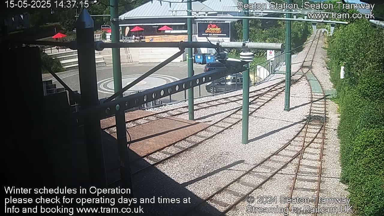 Tram tracks curve through a sunny area with a building and some cars visible.