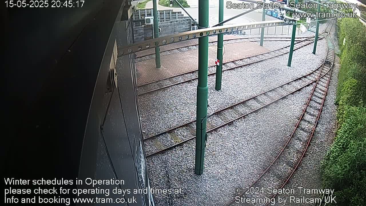 Tram tracks diverge at a station, surrounded by gravel and vegetation.