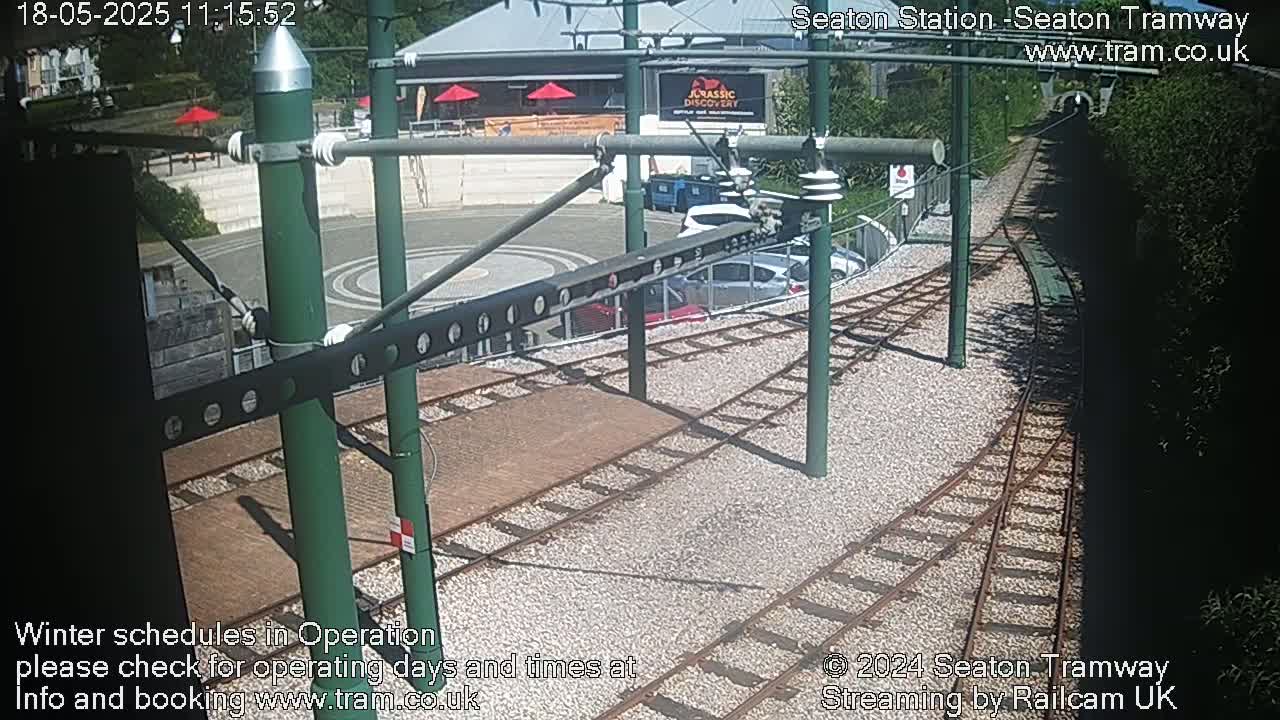 A sunny view of tram tracks and a station platform with parked cars.