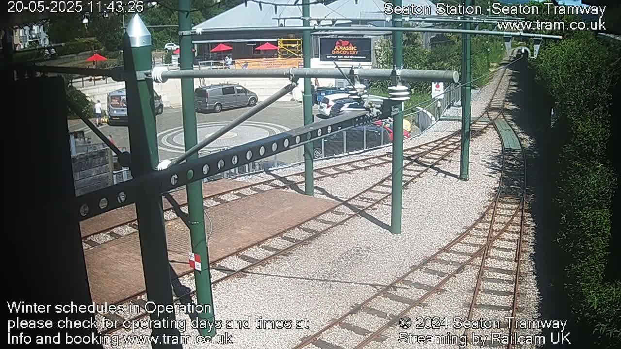 A sunny view of a tramway station with several vehicles parked nearby and train tracks leading into a tunnel.