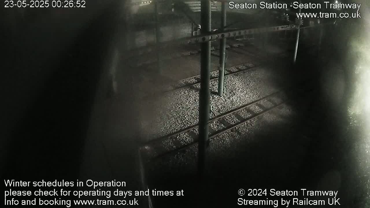 A nighttime, overhead view of train tracks at a station, covered in small stones.