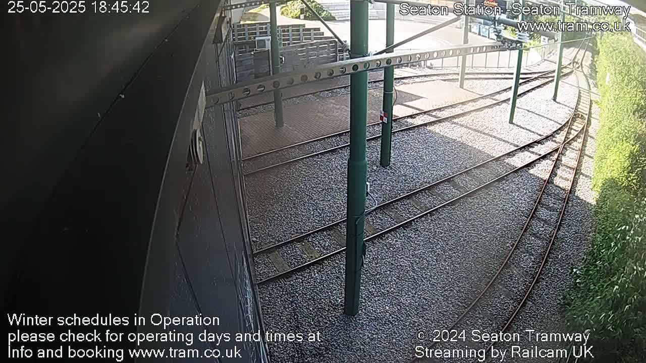 A high-angle view of curving tram tracks on a gravel bed, with supporting poles and a partially visible building.