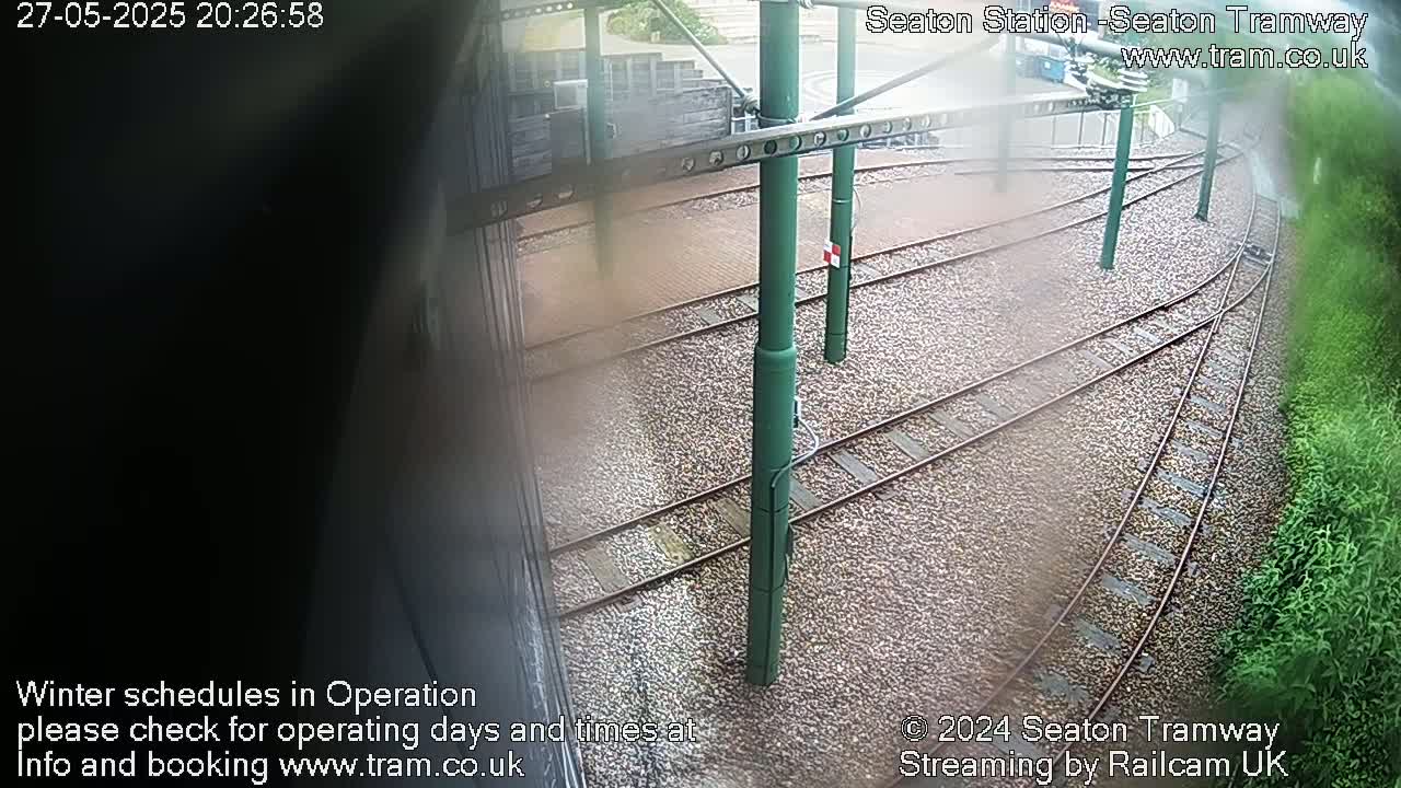 A high-angle, slightly blurry view shows tram tracks curving around a station on a wet, overcast day.