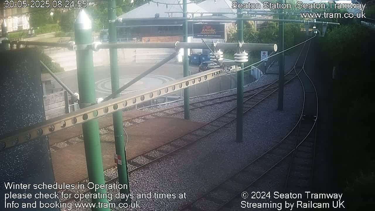 A high-angle view of a tram station's railway tracks and overhead lines on a partly sunny day.