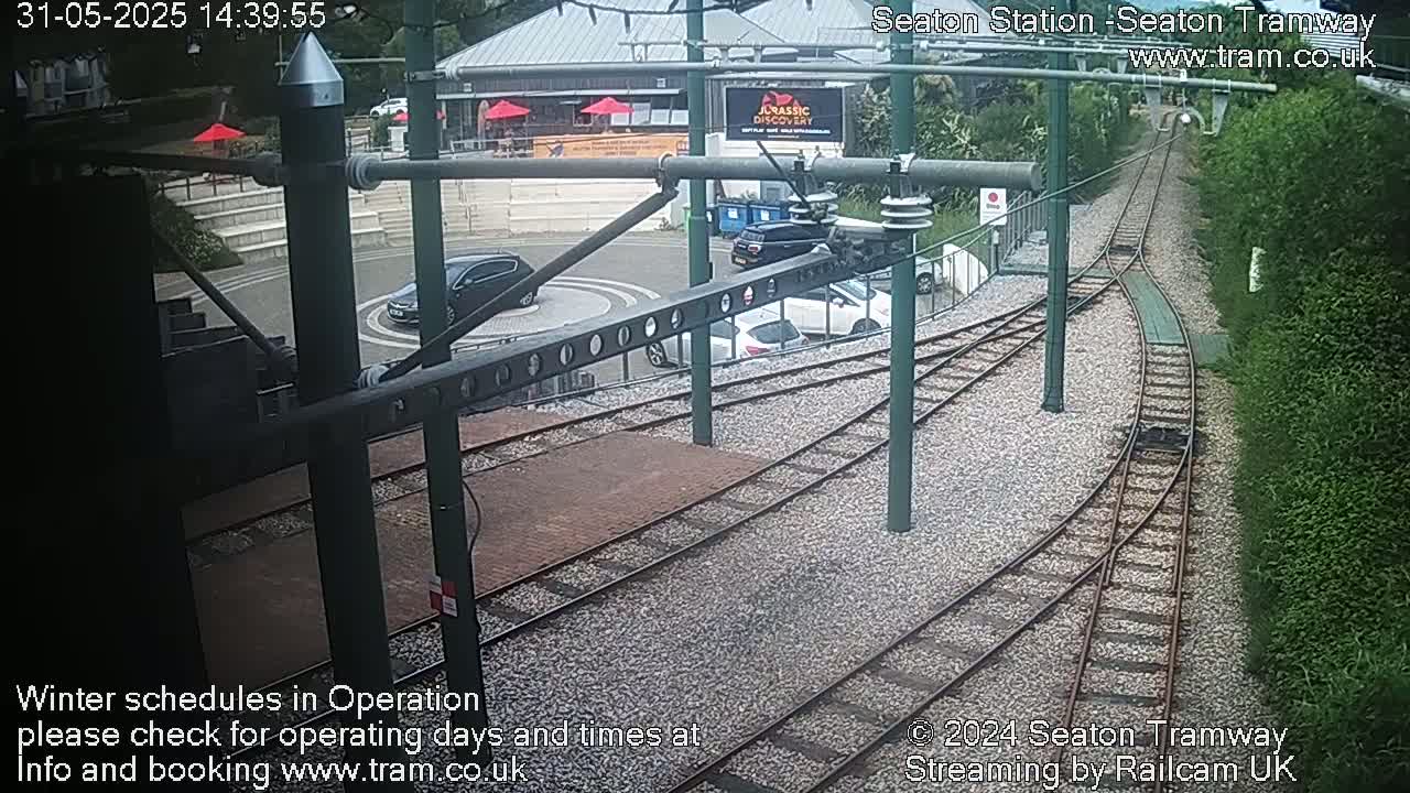 A tram station's turning loop with several cars parked nearby, viewed from an elevated perspective on a sunny day.