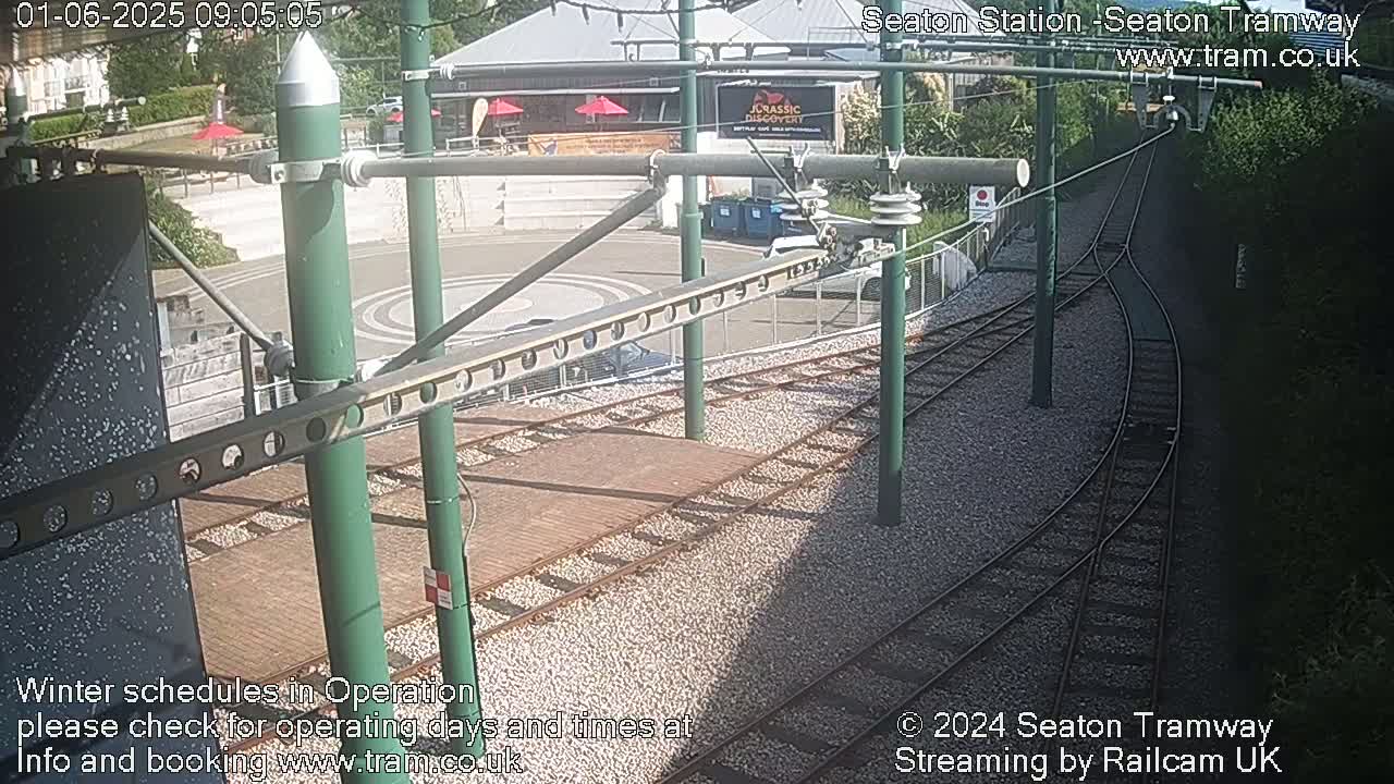 A high-angle view of a tram station platform with train tracks branching off, under sunny conditions.