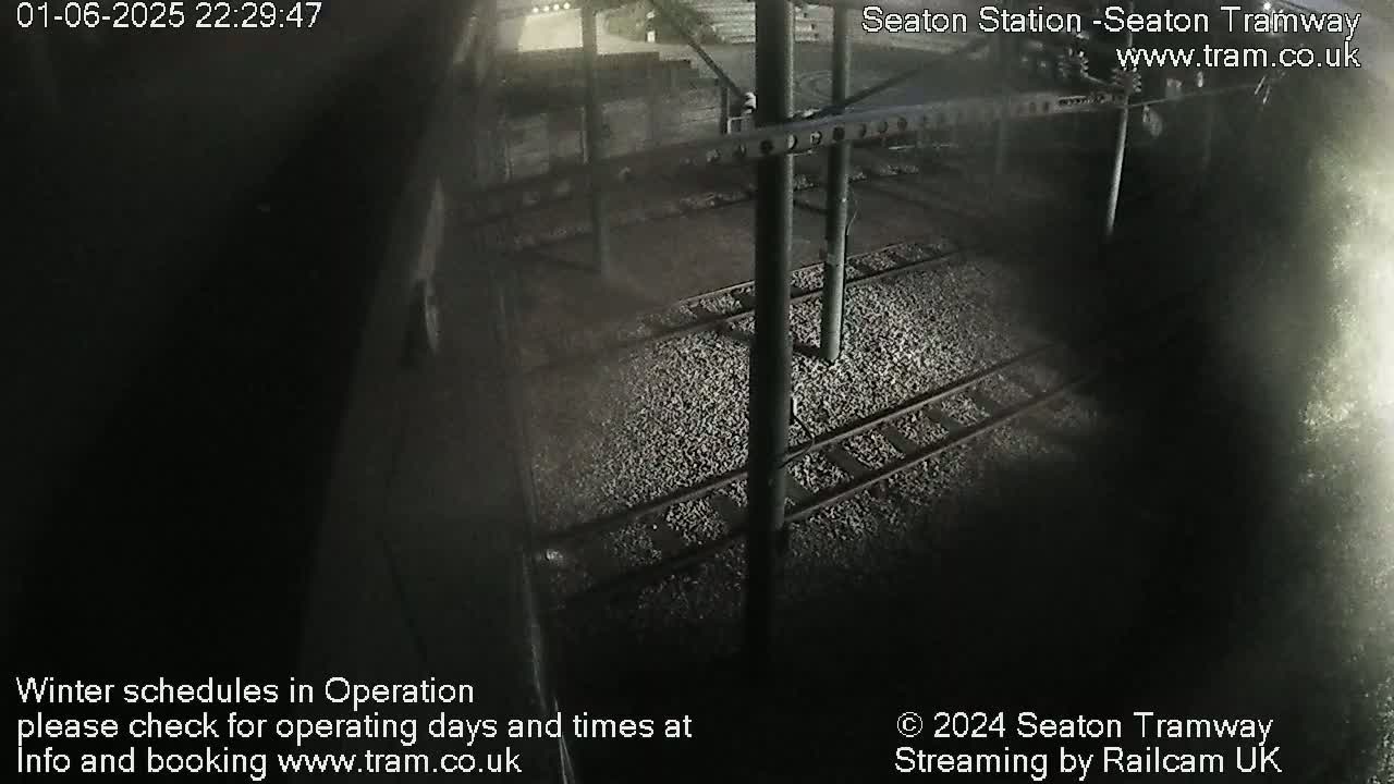 A nighttime, overhead view of train tracks at a station, covered in small stones.