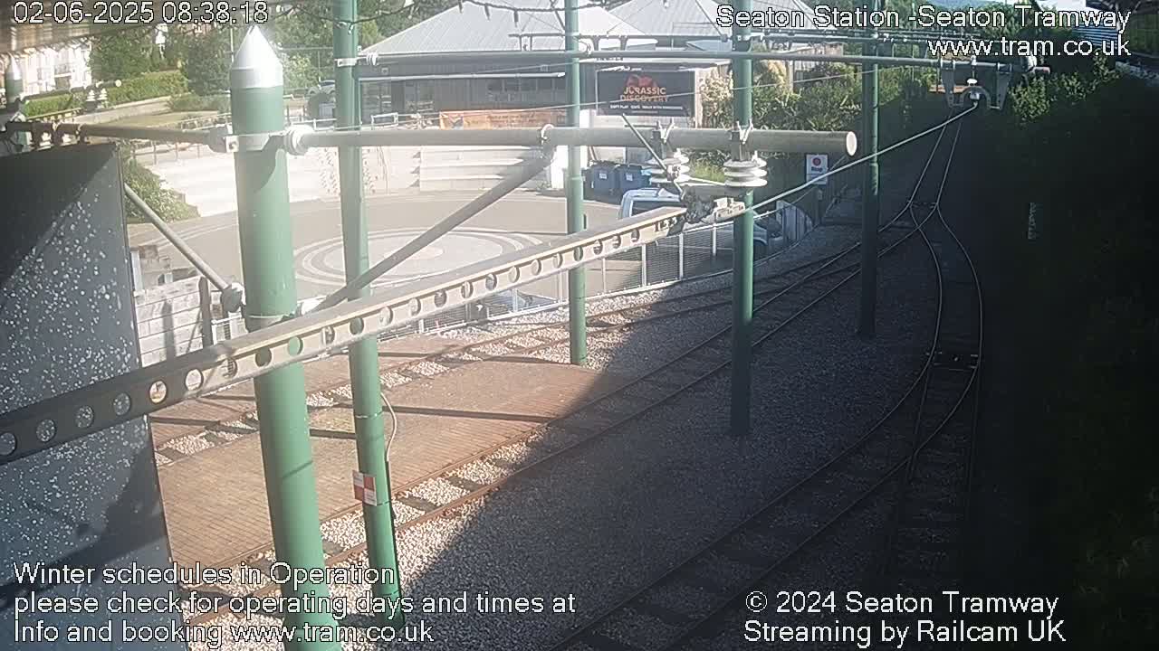 Overhead tram tracks and a station platform are visible in the sunny daylight.