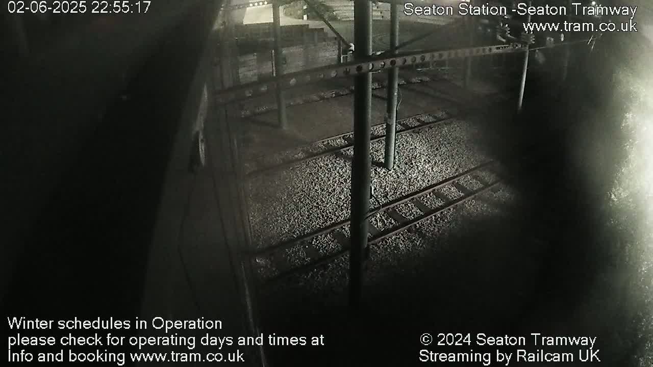 A nighttime, overhead view of train tracks at a station, covered in small stones.