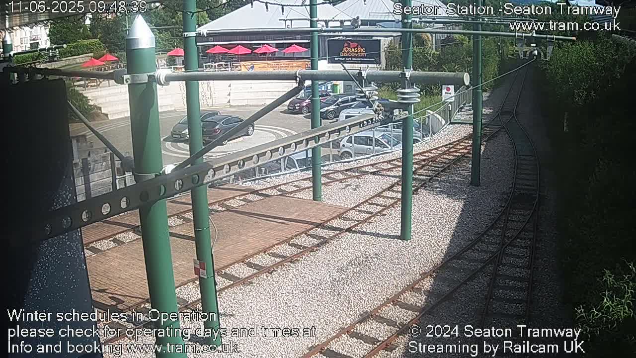 A sunny overhead view of a tram station with several cars parked nearby and tram tracks leading away.