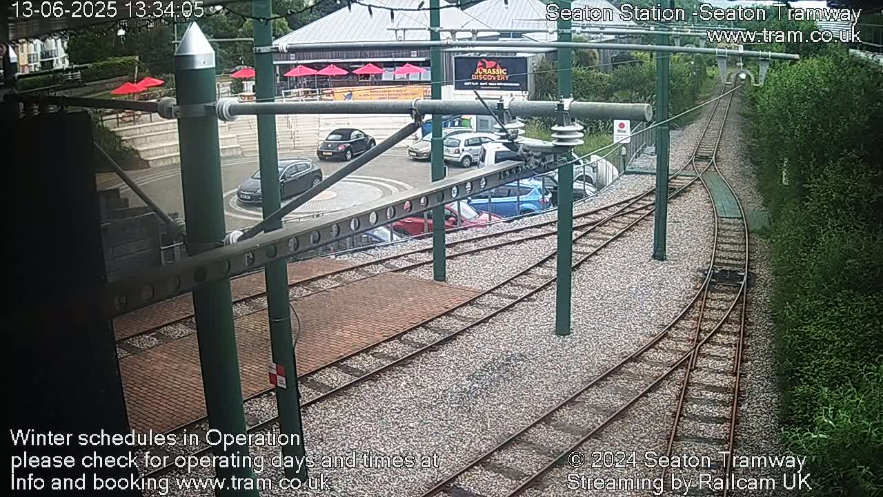 A tramway station with several cars parked nearby, viewed from above on a partly sunny day.