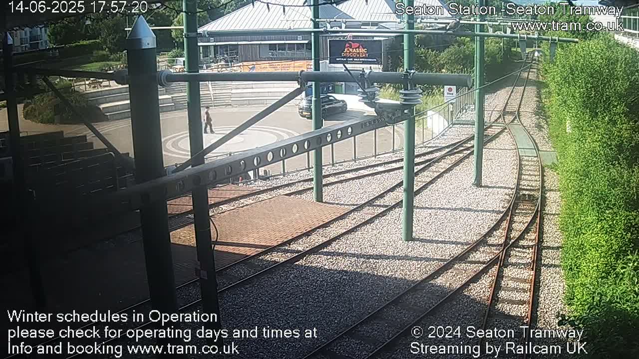 A sunny view of a tram station's curving tracks, a nearby building, and a person walking.