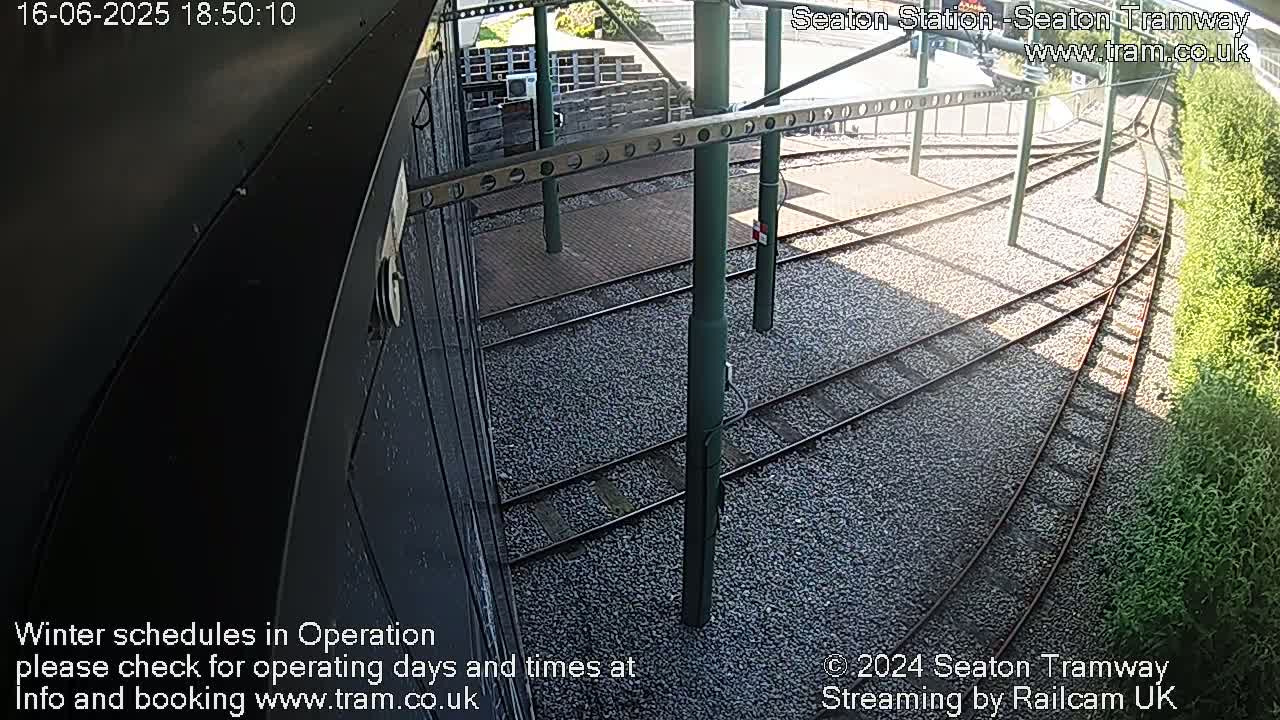 A high-angle, sunny view of train tracks curving away from a station platform.