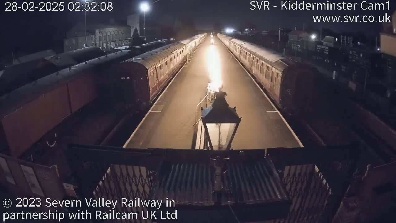 At night, a bright flame illuminates a train track lined with railway cars.