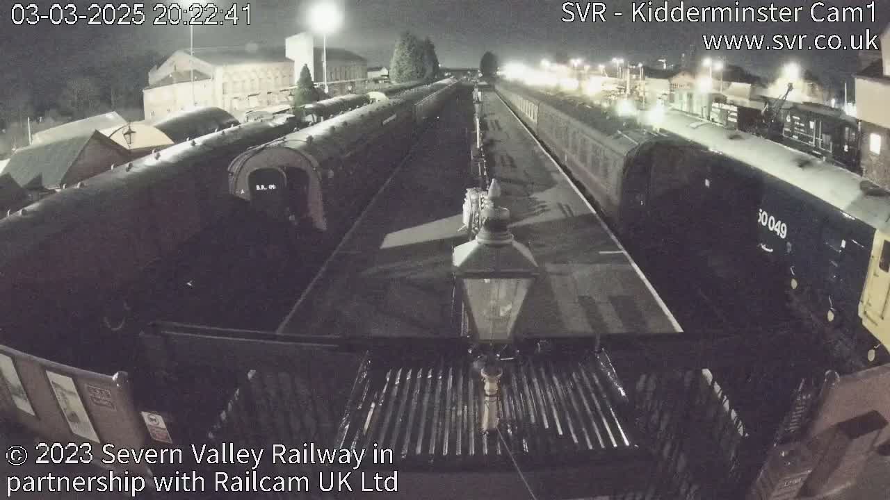 At night, several railway cars are parked on train tracks next to a station.