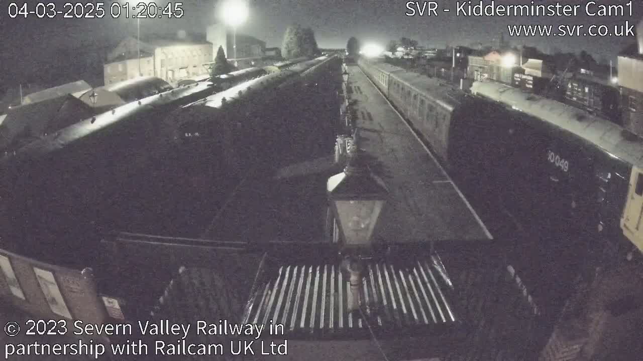 A nighttime view of a train station with numerous railway carriages parked along the tracks under dim lighting.