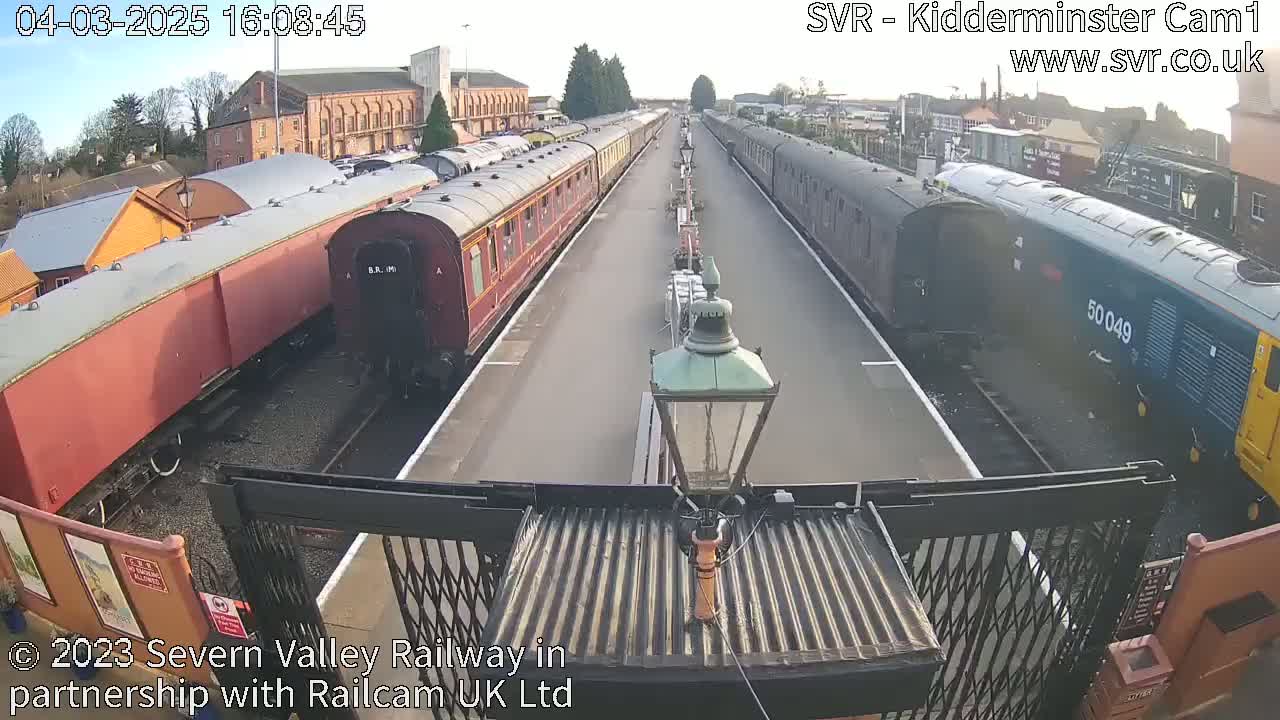 Two long lines of passenger train cars are parked on a railway platform on a sunny day.