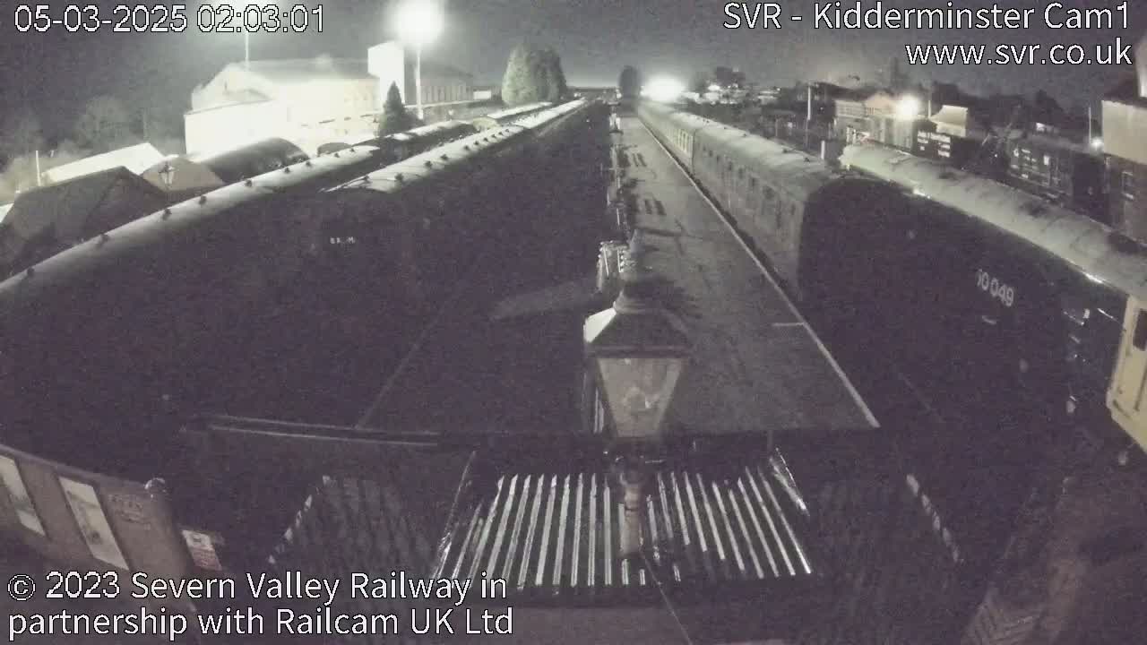 At night, several dark railway cars are parked on tracks at a station.