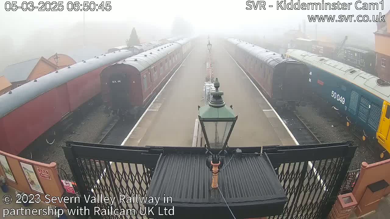 A foggy railway platform with several train cars parked on both sides, and a diesel locomotive at one end.