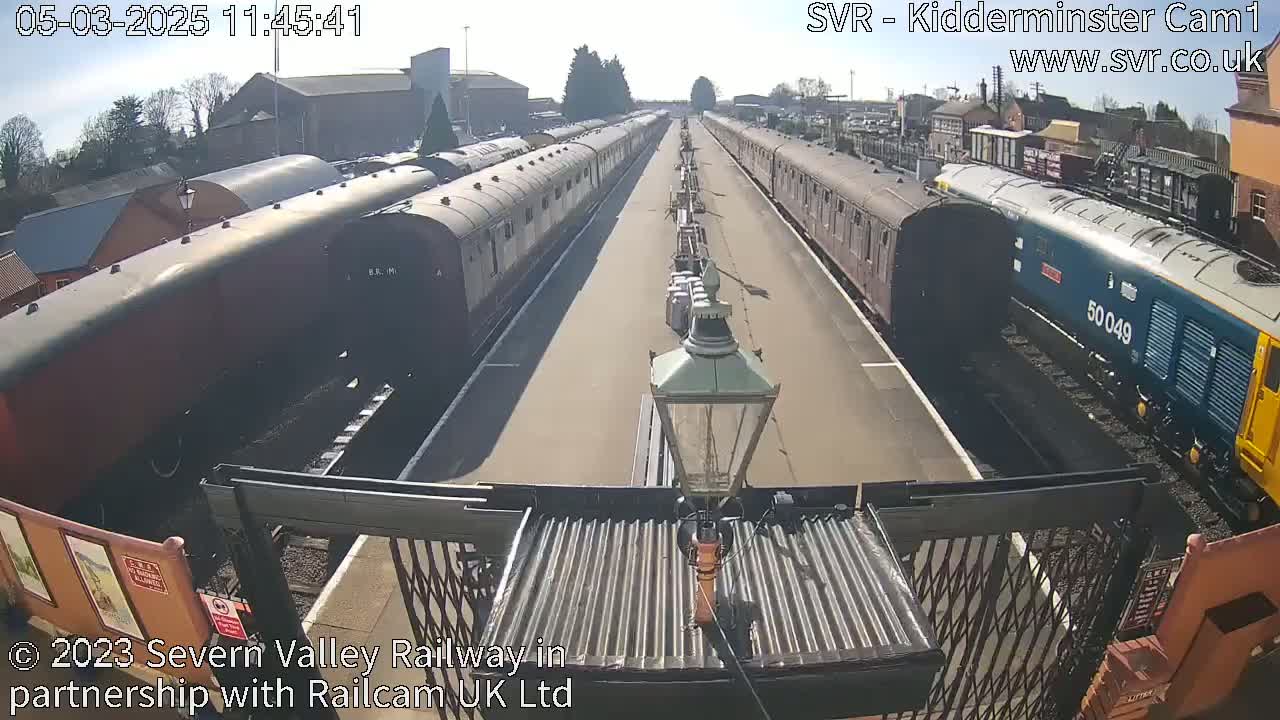 On a sunny day, two lines of railway cars extend from the camera's viewpoint, one dark brown and the other dark blue, with a modern locomotive at the end of one line.