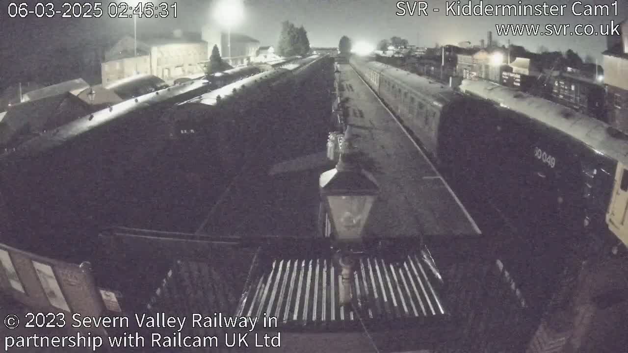 A nighttime view of a railway station with multiple train cars parked on tracks under artificial lighting.