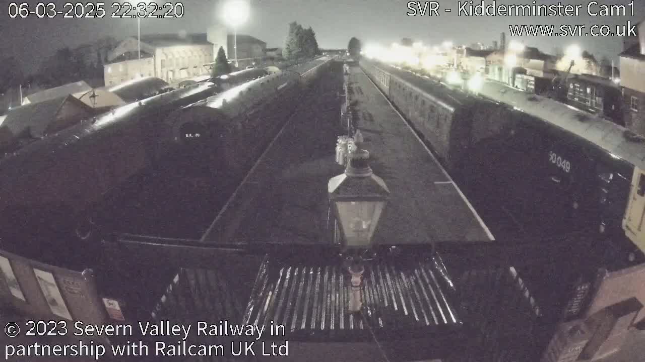 At night, several dark train cars are parked on parallel tracks at a station under dim lighting.