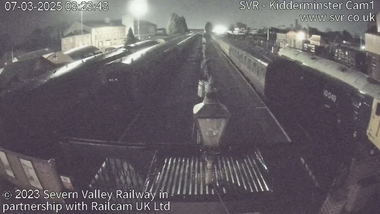 A nighttime view of a train slowly moving through a station, under artificial lights.