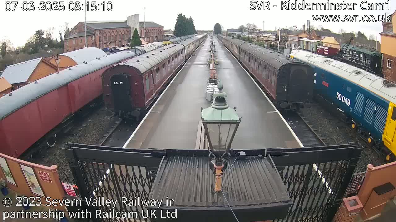 A wet railway platform with long lines of passenger train cars extending into the distance.