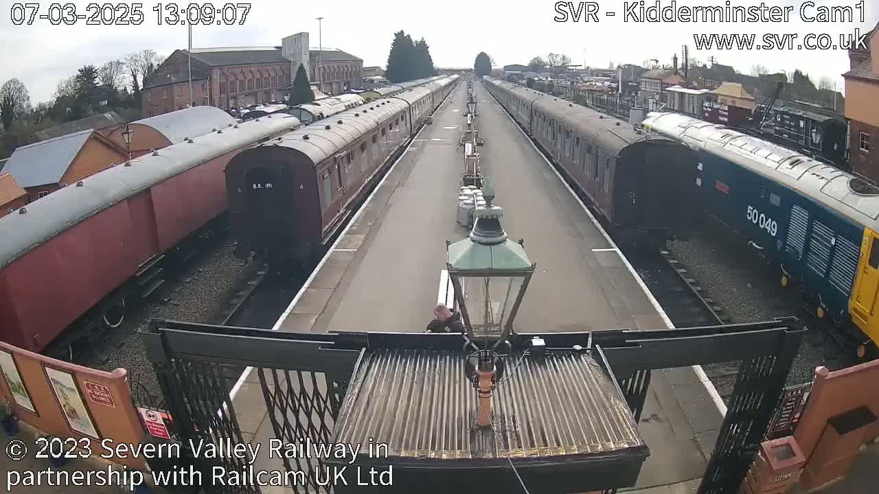 A long line of railway carriages sits on either side of a station platform on an overcast day.