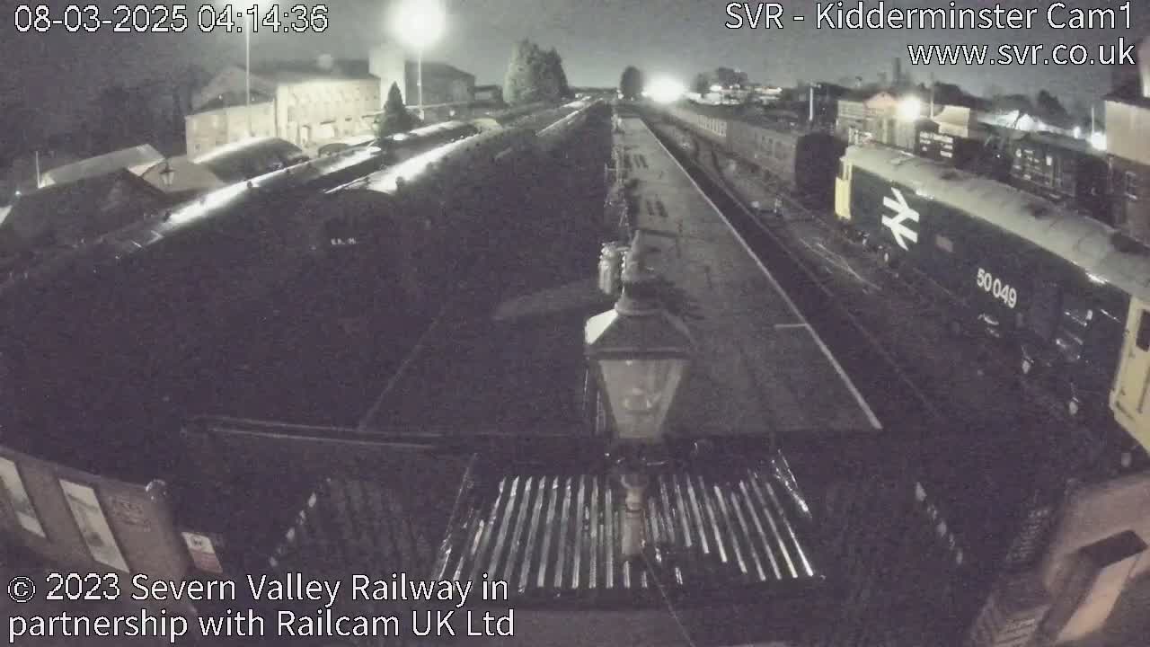 A nighttime view of a train station platform with several train cars and a locomotive parked on the tracks.