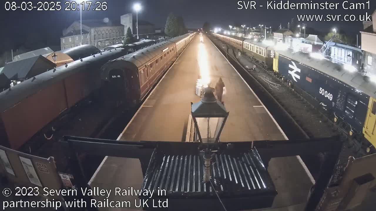 At night, a flame shoots upward between two long passenger trains parked on parallel tracks.