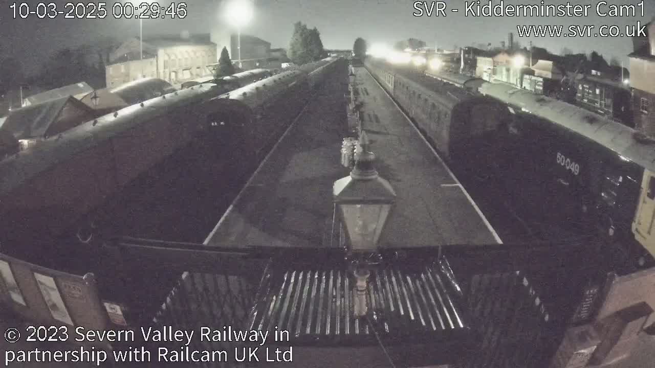 A nighttime view of a railway station with multiple train cars parked on two tracks.